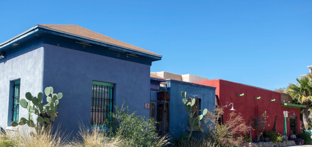 A blue adobe house with prickly pear cactus beside a red building