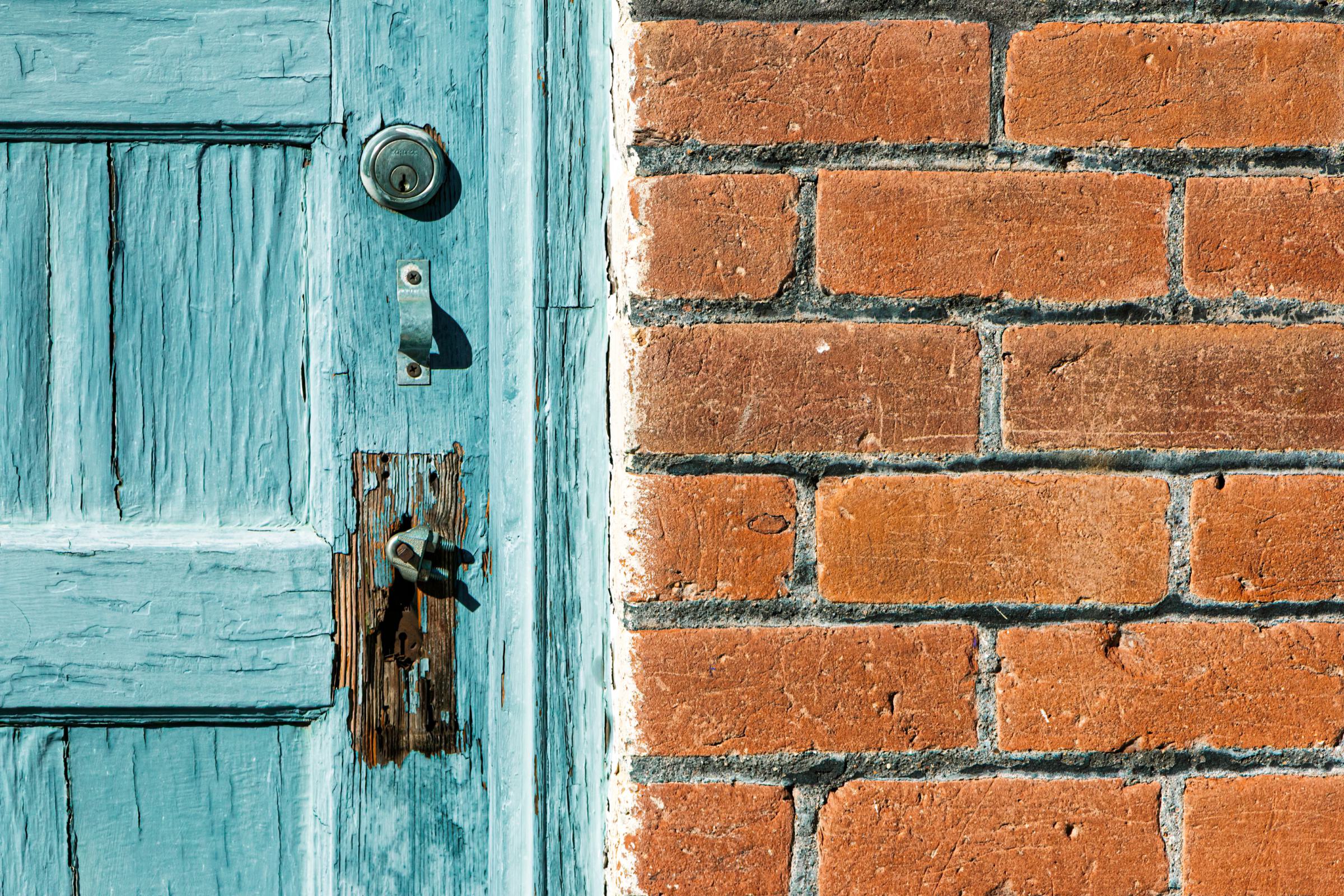 A weathered turquoise door with old locks beside a brick wall